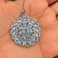 round shaped blue topaz and cubic zirconia studded silver pendant displayed on hand