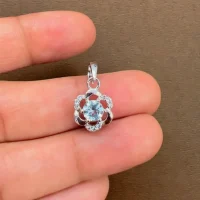 5mm round blue topaz with cubic zirconia flower shaped silver pendant displayed on hand