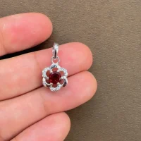 5mm round garnet with cubic zirconia flower shaped silver pendant displayed on hand