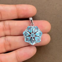 5x7 pear shaped blue topaz with cubic zirconia flower shaped silver pendant displayed on hand
