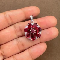 5x7 pear shaped garnet with cubic zirconia flower shaped silver pendant displayed on hand