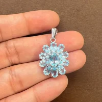 silver pendant flower shaped with blue topaz displayed on hand