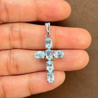 silver pendant cross design with 4x6mm oval blue topaz displayed on hand