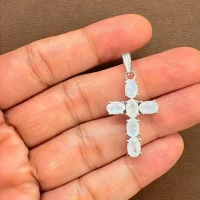silver pendant cross design with 4x6mm oval rainbow moonstone displayed on hand