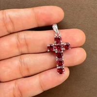 silver pendant cross design with 5mm round garnet displayed on hand