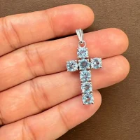 silver pendant cross design with 5mm round blue topaz displayed on hand