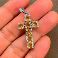 silver pendant cross design with 5mm round blue topaz displayed on hand