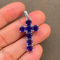 silver pendant cross design with 5mm round blue topaz displayed on hand