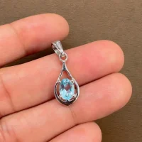 silver pendant with 5x7 mm oval shaped blue topaz displayed on hand