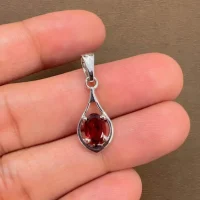 silver pendant with 5x7 mm oval shaped garnet displayed on hand