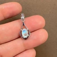 silver pendant with 5x7 mm oval shaped rainbow moonstone displayed on hand