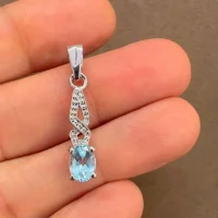silver pendant with 5x7 mm oval blue topaz displayed on hand