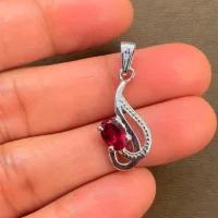 silver pendant with 5x7 mm oval garnet displayed on hand