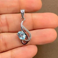 silver pendant with 5x7 mm oval blue topaz displayed on hand