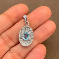silver pendant with 5x7 mm oval blue topaz displayed on hand