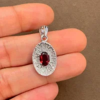 silver pendant with 5x7 mm oval garnet displayed on hand