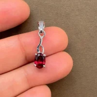 silver pendant with 5x7 mm oval garnet displayed on hand