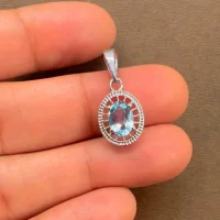 silver pendant with 5x7 mm oval blue topaz displayed on hand