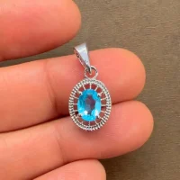 silver pendant with 5x7 mm oval swiss blue topaz displayed on hand