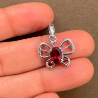 silver pendant butterfly shaped with 5x7 mm oval garnet displayed on hand