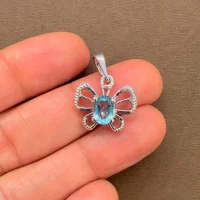 silver pendant butterfly shaped with 5x7 mm oval blue topaz displayed on hand
