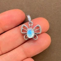 silver pendant butterfly shaped with 5x7 mm oval rainbow moonstone displayed on hand