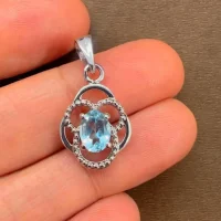 silver pendant with 5x7 mm oval blue topaz displayed on hand