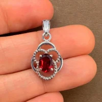 silver pendant with 5x7 mm oval garnet displayed on hand