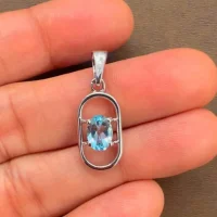 silver pendant with 5x7 mm oval blue topaz displayed on hand