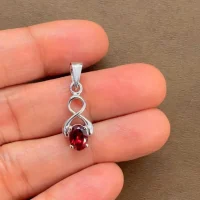 silver pendant with 5x7 mm oval garnet displayed on hand