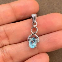 silver pendant with 5x7 mm oval blue topaz displayed on hand