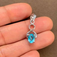 silver pendant with 5x7 mm oval swiss blue topaz displayed on hand