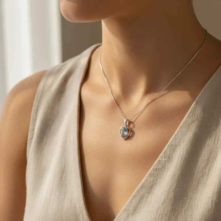 model wearing silver pendant heart shaped with 6x4 mm oval blue topaz