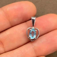 silver pendant heart shaped with 6x4 mm oval blue topaz displayed on hand