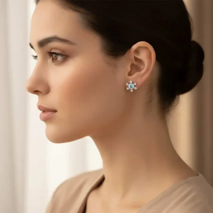 model wearing silver studs snowflake design with 5 mm round blue topaz in band setting and cubic zirconia in prong setting