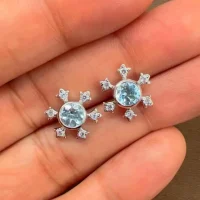 silver studs snowflake design with 5 mm round blue topaz in band setting and cubic zirconia in prong setting displayed on hand
