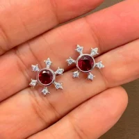 silver studs snowflake design with 5 mm round garnet in band setting and cubic zirconia in prong setting displayed on hand