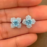 Silver Studs flower shaped with 6mm round shaped Blue Topaz Gemstone and Cubic Zirconia displayed on hand