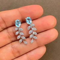 silver earrings gemstones with 5x7 mm oval blue topaz displayed on hand