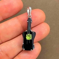 silver carved gemstone pendant with guitar shaped black onyx and peridot displayed on hand